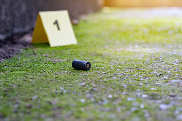 Pistol bullet shell and blurred number 1 on yellow paper on cement floor which has bright green...