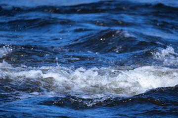 Sea waves with white foam are on blue shore water