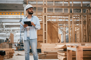 Fototapeta premium Unfinished project, holding digital tablet. Industrial worker in wooden warehouse