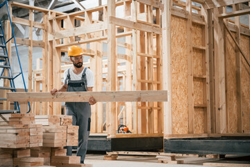 Fototapeta premium Going and carrying plank. Industrial worker in wooden warehouse