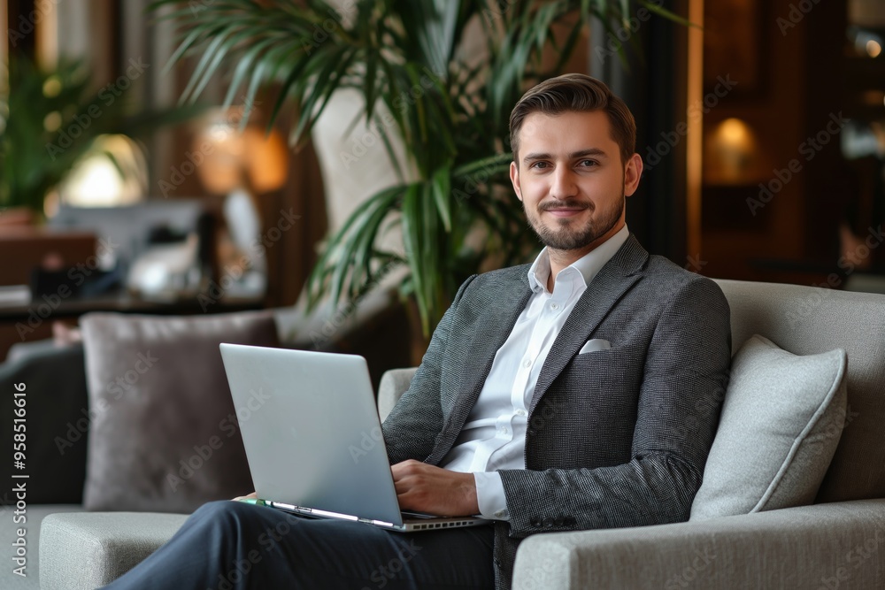 Poster a man in a suit is sitting on a couch with a laptop in front of him. he is smiling and he is enjoyin