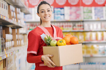 Smiling supermarket clerk holding a box full of groceries