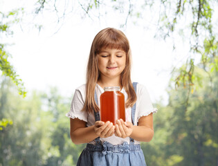 Happy little girl holding a jar of honey outdoors