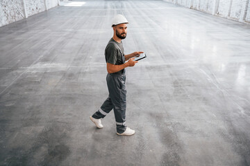 Side view, using digital tablet. Male worker is in the empty warehouse