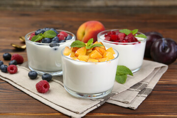Tasty yogurt with fresh berries, fruits and mint in glasses on wooden table, closeup