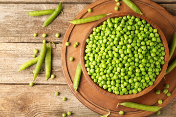 Fresh green peas in bowl and pods on wooden table, flat lay