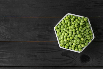 Fresh green peas in bowl on black wooden table, top view. Space for text