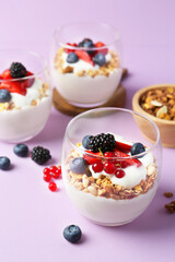 Tasty yogurt with fresh berries and granola in glasses on violet background, closeup