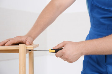 Worker with screwdriver assembling furniture indoors, closeup