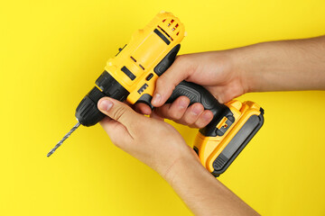 Man with cordless electric drill on yellow background, closeup