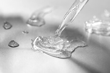 Dripping cosmetic serum from pipette on grey background, closeup