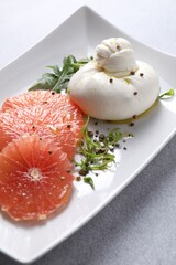 Delicious burrata cheese, grapefruit and spices on light grey table, closeup