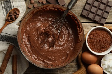 Chocolate dough in bowl among ingredients on wooden table, flat lay