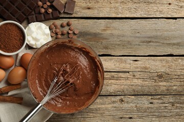 Chocolate dough in bowl and ingredients on wooden table, flat lay. Space for text