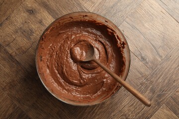 Chocolate dough in bowl and spoon on wooden table, top view