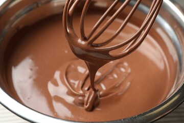 Chocolate dough dripping from whisk into bowl on table, closeup