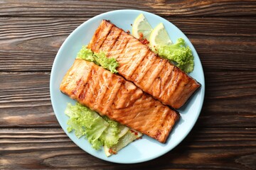 Delicious grilled salmon fillets with lettuce and lemon on wooden table, top view