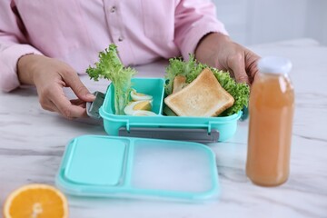 Woman packing school lunch box with healthy meal at white marble table in kitchen, closeup