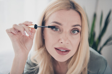 Fototapeta premium Close up photo of pretty young woman apply mascara silky pajama white interior bedroom apartment indoors