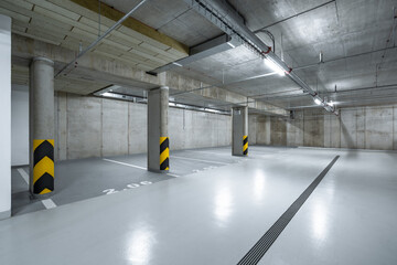 An empty underground parking garage with concrete walls, floors, and columns, yellow and black...