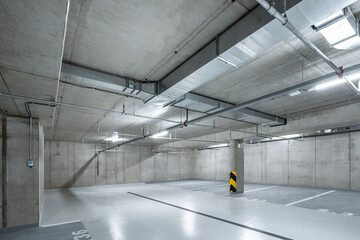 Spacious underground parking garage with industrial lighting and concrete walls, showing modern architectural design with visible installations and clean floor spaces.