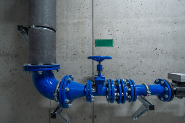 A close-up of a blue industrial water valve and pipes attached to a concrete wall, highlighting engineering and plumbing elements in an industrial setting.