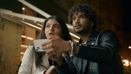 Confused puzzled man woman tourist travelers in night evening city Indian Arabian couple lost in street town travel tour trip guy girl using mobile phone navigator app online map GPS navigation point