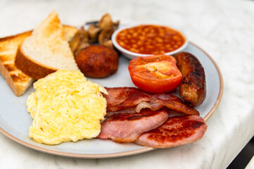 Full English Breakfast with sausage, mushrooms, tomato, bacon, homemade hash brown, baked beans, scrambled eggs and toast bread with butter