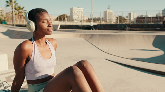 Close-up side view of the girl athlete with headphones chilling at the skate park