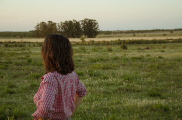 joven mujer de espaldas contemplando un basto campo en un atardecer despejado
