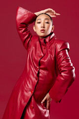 Fashionable asian brunette woman in a red leather coat posing with hands on hips and head tilted to the side