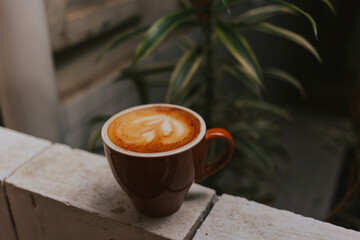 Cappuccino with foam in a red mug on a concrete background