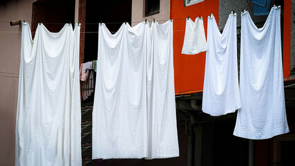 Freshly washed white sheets hanging on clothesline outside, swaying in breeze against building...