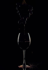 dripping red wine from a bunch of grapes into a glass of wine