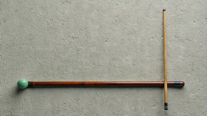 A green billiard ball and two pool cues on a grey surface