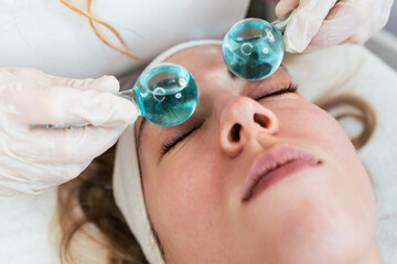 Beautiful young woman enjoying in cryotherapy with cryo sticks or ice globes. Modern and popular...
