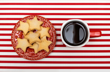 Star shaped cookies on red plate next to red coffee cup, red and white striped background, top view