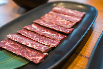 Premium fresh raw sliced Wagyu beef with marbled on black plate for grilled beef at Yakiniku restaurant background. A5 Yakiniku Wagyu beef sirloin served to Japanese barbecue grill, shabu or sukiyaki.