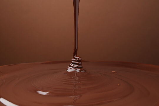 Pouring delicious melted chocolate on brown background, closeup