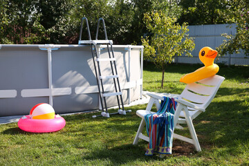 Above ground swimming pool, folding chair, towel, inflatable rings and ball in backyard