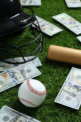 Baseball ball, bat, helmet and dollar banknotes on green grass outdoors