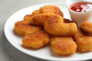 Tasty chicken nuggets with chili sauce on grey table, closeup