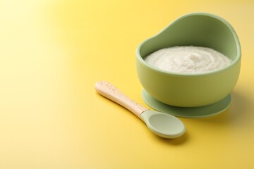 Delicious baby food in bowl and spoon on yellow background. Space for text