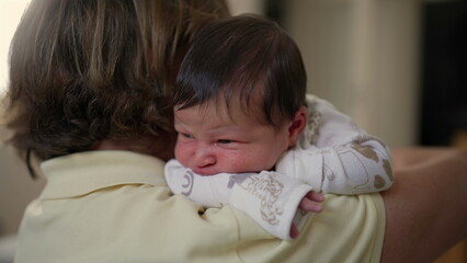 Close-up of a newborn baby resting on grandmother's shoulder, highlighting tender moments of...