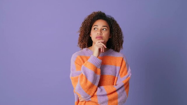 Young woman can't make decision looking at camera on lilac background in studio