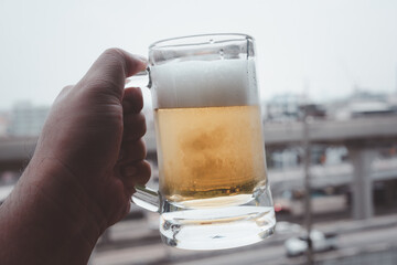 The person holding a beer cup with foam on top in the condominium on a sunny day