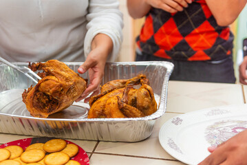 An unrecognizable person serves roast chicken on a metal tray during a meal. The close-up captures the warmth of a home-cooked dish being shared, emphasizing family togetherness. 
