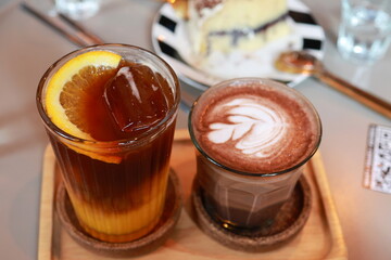 Orange Black Coffee served with hot latte art on a wooden tray. Orange Juice and coffee, oranges cut thin pieces with Ice and Coffee has milk foam whipped until fine, Micro Foam size to draw patterns
