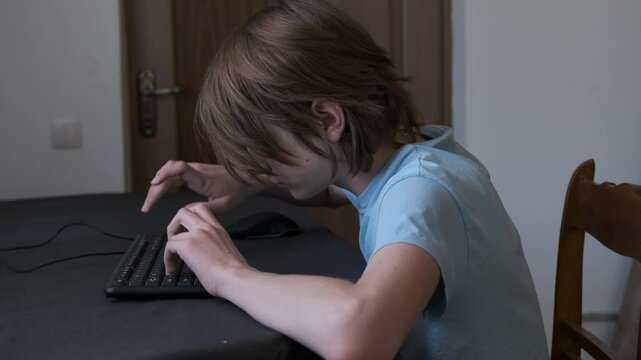 Young man is sitting at a table typing on a keyboard, he is hunched over and developing bad posture