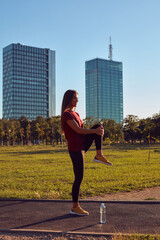 Young woman stretching after exercise and jogging in urban park during sunny summertime day.